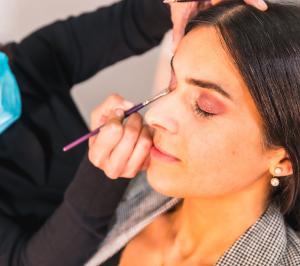 Woman performing makeup services on a woman with her eyes closed.