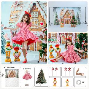 Child in red-and-white striped dress posing with gingerbread house backdrop, candy-themed props, and Christmas decorations in a holiday photo setup kit.