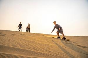 A family watches as their son surfs on a sand dune.