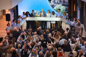 A ribbon-cutting ceremony at UNC Kenan-Flagler Business School with dignitaries and students on stage holding a large ceremonial ribbon that reads 'GRAND OPENING CELEBRATION.' The event takes place in a modern auditorium with a large screen displaying the