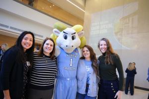Four people posing for a photo with Rameses, the UNC mascot, at the Steven D. Bell Hall Grand Opening Celebration event inside the building.