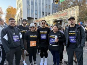 Six HomeFirst employees pose for a photo at Turkey Trot Silicon Valley 2024 wearing running bibs and shirts that say "housing is a human right"
