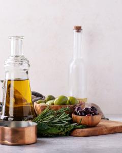 Glass bottle of extra-virgin olive oil surrounded by herbs on a wooden board, representing Mediterranean ingredients used in Demeter’s Pantry’s clean-label cooking.