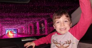 A child show his holiday spirit with an arm pumped in the air while in his family vehicle is driven through a light tunnel Glittering Lights at Las Vegas Motor Speedway.