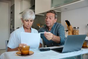 Two people looking over bills and financial paperwork at home with a laptop and calculator
