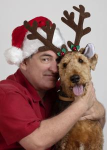 a man wearing a Santa hat with a dog wearing reindeer antlers
