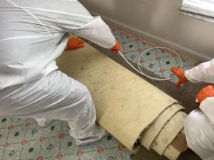 Two SERVPRO technicians in white protective suits and orange gloves removing contaminated flooring material during biohazard cleanup in Naples, Florida