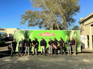 SERVPRO of Naples/Marco Island team of ten technicians in black uniforms standing in front of large green branded truck at company facility