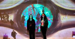 Image of two artists with a video projected onto them.