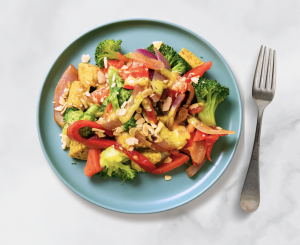 A serving of Demeter’s Pantry’s vegan Coconut Curry Grilled Tofu with Brown Rice, featuring broccoli, red peppers, onions, and sliced almonds on a blue plate, styled against a light marble background.
