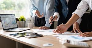 Hands of a strategy team reviewing charts, analytics reports, and campaign plans across a collaborative workspace.
