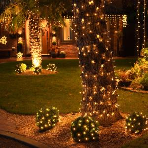 Warm fairy lights wrapped around trees and shrubs in a glowing yard.