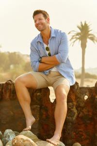 Wellness expert, Gordon Fraser, smiles broadly into the soft summer light while leaning against the pier at Malibu beach.