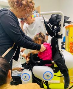 RoboCT trainer instructs a clinic therapist on fitting a child into the KidGo paediatric lower-limb exoskeleton during a supervised setup session in Pisa.
