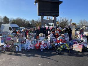 a large pile of holiday gifts surrounded by smiling workers and community members for We Buy Any House Fast's annual Toys for Tots Toy Drive