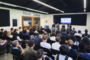 Audience seated in a large room facing four panelists speaking on stage at Menlo College’s Institute of AI and Sustainability, with a presentation screen displayed behind them. Photo is taken from the back of the room, highlighting the crowd and event spa