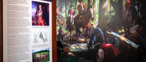 A historical display featuring a painting of soldiers on horseback in a forest, with accompanying text and illustrations on the left.