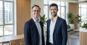 Two Arrel founders standing indoors in business attire, smiling, with a modern office background.