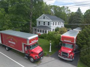 Aerial view of two red Philip P. Massad Movers trucks parked in front of a white house during a moving job