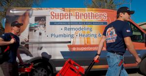 Two Super Brothers Plumbing Heating and Air technicians walking with tools in front of a branded service van during a Bay Area home electrification project.