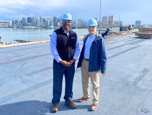 Fernando Harris and Chuck Moratz on the flight deck of the USS Carl Vinson with San Diego Bay and the San Diego skyline in the background.