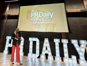 Erica Hakonson stands on stage holding the PR Daily 2025 Top Agency of the Year (Small Agency) award, with large illuminated “PR DAILY” letters and the Ragan PR Daily Awards screen behind her.