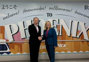 Chairman Shing-Hwang (George) Kao of China Airlines and Phoenix Mayor Kate Gallego stand in front of a colorful “Welcome to Phoenix” mural, smiling and shaking hands at Phoenix Sky Harbor International Airport.