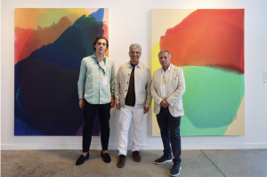 Photo of three men posing in front of paintings
