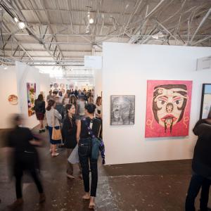 Crowds walking through the San Francisco Art Fair, viewing contemporary artworks displayed across multiple gallery booths inside a bright industrial exhibition hall.