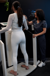 A MetaLab technician assists a patient standing on the SECA Body Composition Analyzer, ensuring proper hand and foot electrode contact for accurate bioimpedance measurements during the scan.