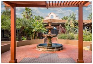 Courtyard at Origins Texas Recovery featuring a tiered fountain surrounded by tropical plants, brick walkways, and Spanish-style buildings in the background.