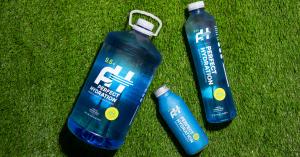 Perfect Hydration Gallon, 1 Liter and Aluminum Bottle with sustainability badges on grass backdrop