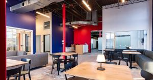 Interior view of Elevator’s North Kansas City common area with tables, couches, colorful walls, and open industrial ceilings designed for coworking.