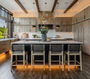 Wide view of Suncadia kitchen interior design by Ariana Designs & Interiors featuring a black island, wood cabinetry, and pendant lighting.