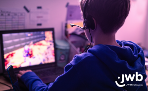 A boy wearing a headset, facing away from the camera, playing a video game on a laptop