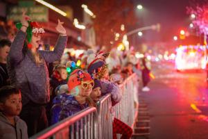 Adults and children in festive clothing watching a parade at night.