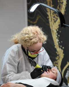 Alla Yesinovskiy performing a permanent makeup procedure on a client at Allegria Studio in Aurora, Ohio, wearing protective gear.