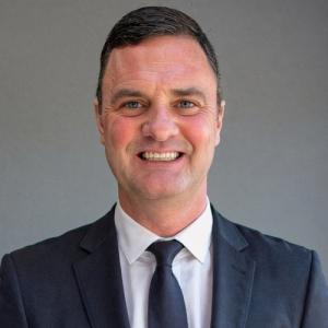 Jason Baumgartner, Azra AI’s Vice President of Clinical Trials & Life Sciences, smiling and wearing a dark suit and tie against a neutral background.