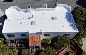 "Aerial view of a completed white TPO commercial flat roof installation in San Francisco, featuring skylights and reflective energy-efficient membrane by Lifetime Roofing & Renovation."
