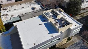 Aerial view of a completed white TPO commercial flat roof in San Francisco featuring skylights and a reflective energy-efficient surface, installed by Lifetime Roofing & Renovation.