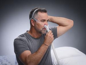 A middle aged man with salt and pepper hair putting on his DeltaWave™ CPAP mask system before going to bed.