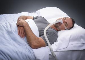 A middle aged man with salt and pepper hair, blissfully sleeping on his side while wearing the REMSleep Holdings DeltaWave™ CPAP mask system..