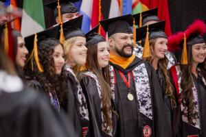 male and female students in caps and gowns pose for a photo