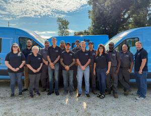 A large group of Tru Plumbing and Gas employees, smiling and standing in front of branded blue vans