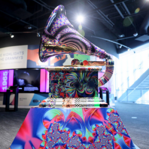 A vibrant, psychedelic Grammy trophy stands prominently in a modern exhibition space, with colorful patterns and reflections.