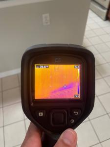 Thermal imaging camera displaying temperature variations on a wall and floor to detect hidden moisture.