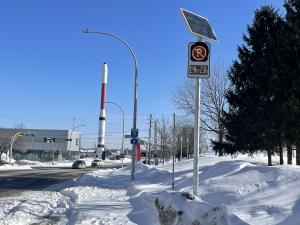 Solar-powered dynamic parking sign in Laval displaying time-based parking restrictions along a snow-covered roadway.
