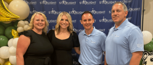 Four individuals pose together in front of a Starlight backdrop, featuring balloons and decorations in green, white, and gold.