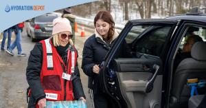Volunteer wearing a Red Cross vest hands bottled water supplied by Hydration Depot to a resident at a vehicle during emergency water distribution in Waterbury Connecticut.