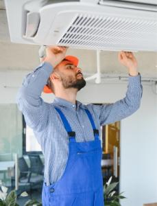 HVAC technician in safety gear performing maintenance on a commercial ceiling cassette air conditioner for Easy Fix HVAC.